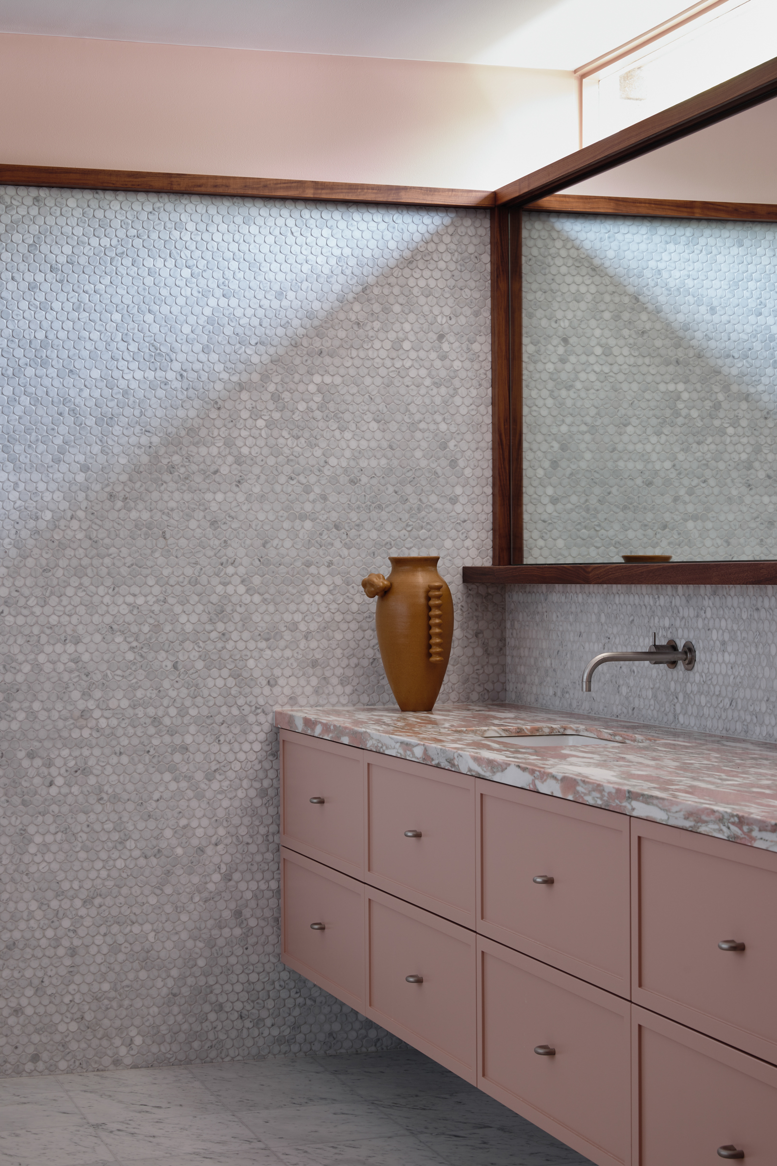 A bathroom with pink marble counter tops, and intricate white tiled walls and a celestory window.