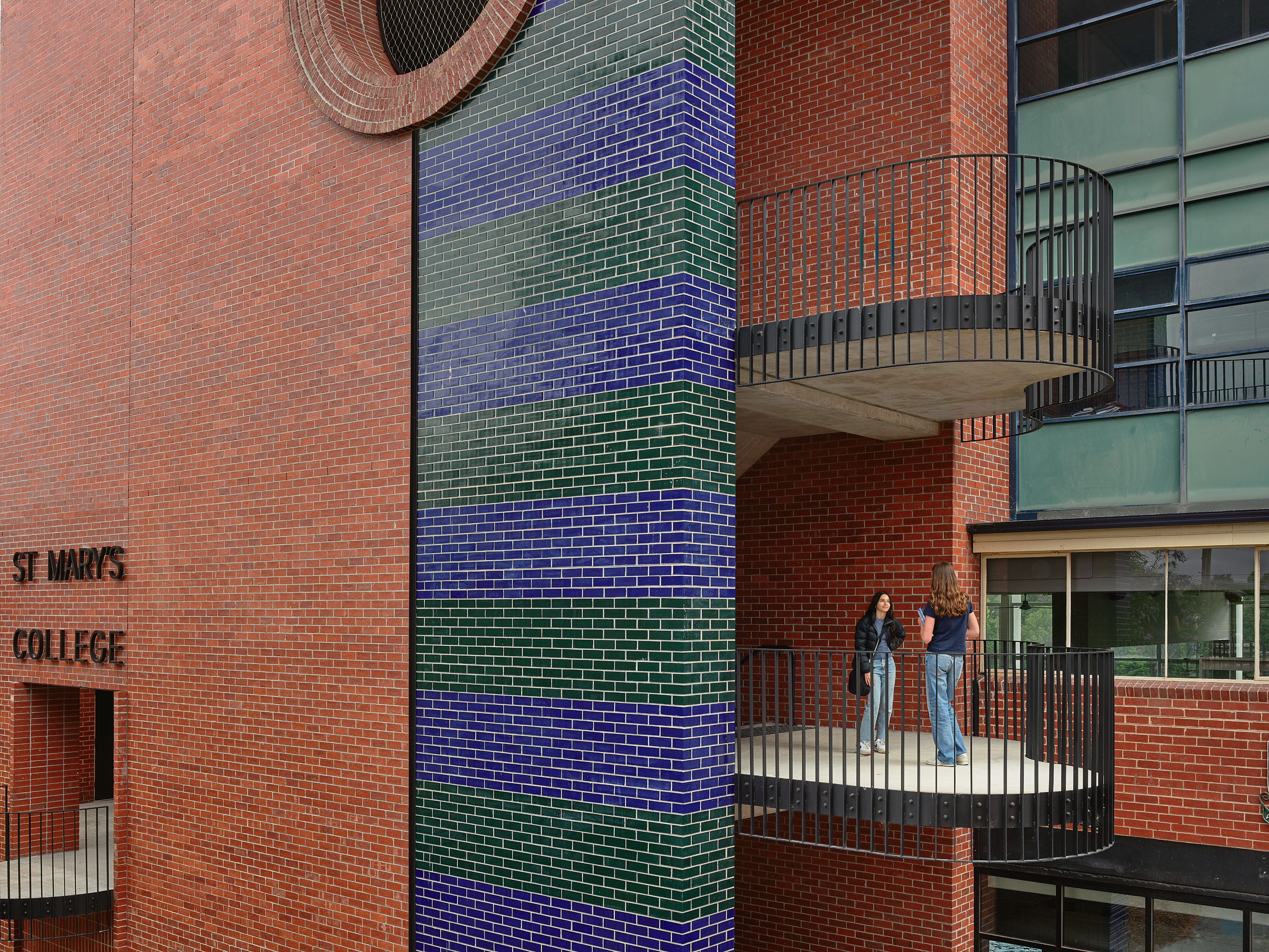 a red, blue and green brick building with a staircase, and two people chatting.