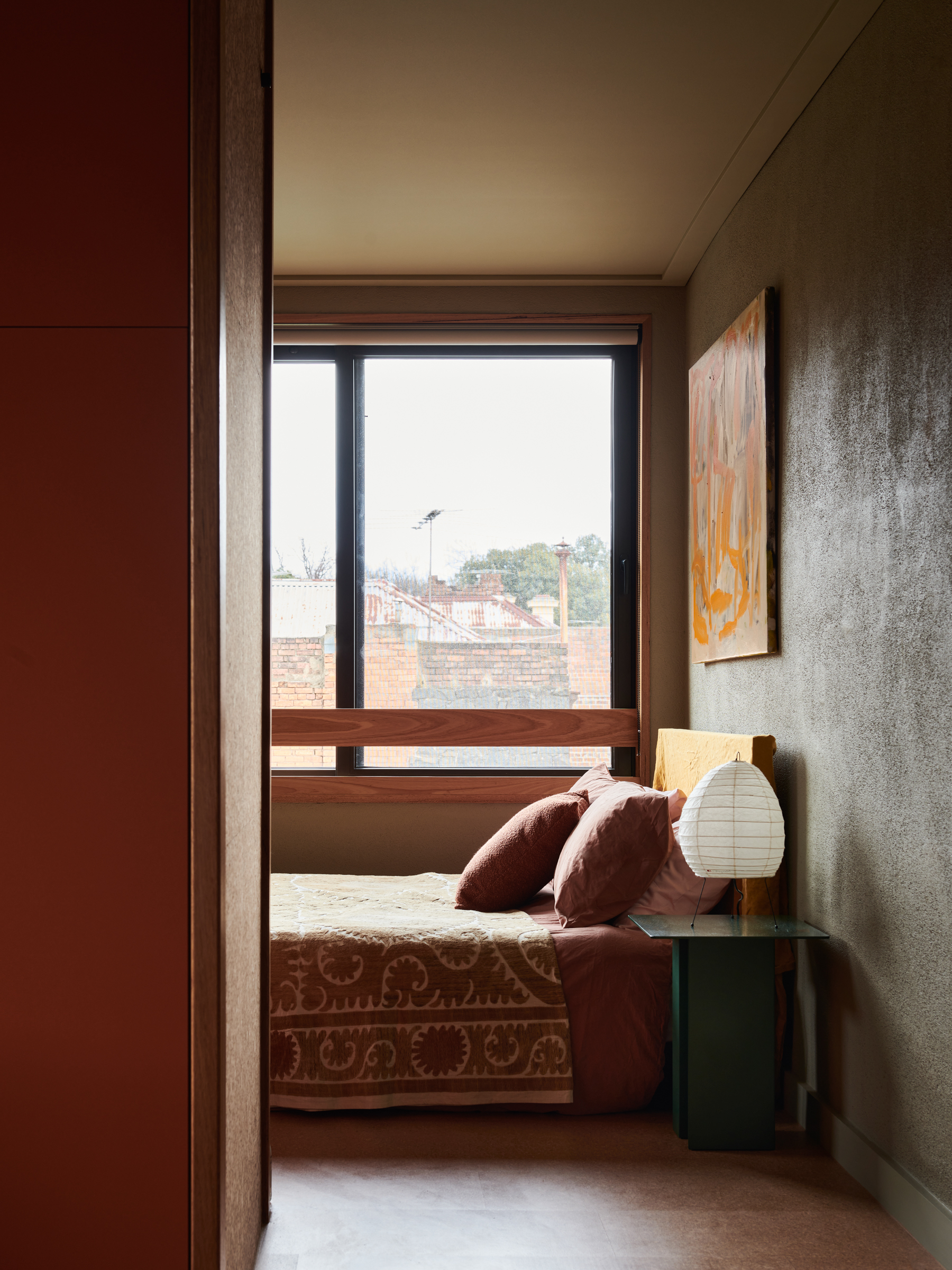 A bedroom with a bedside table, lamp and a window.